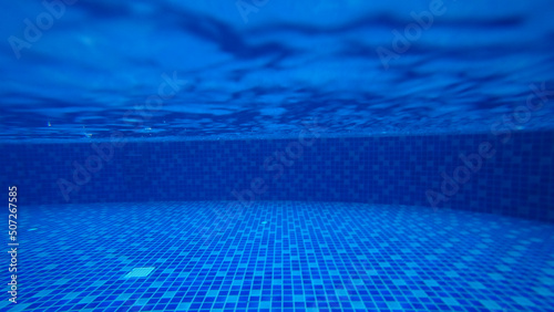 Raindrops on the surface of the pool water. An unusual angle from under the water. Vibration from drops. Large splashes and circles under the water. Turquoise and blue tile swimming pool