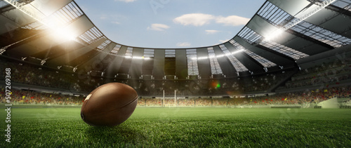 Leather american football ball on grass of football field at stadium with spotlight. Concept of sport, art, energy, power