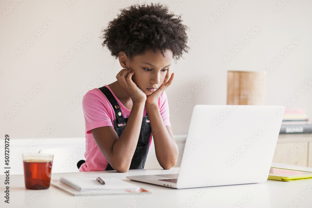Serious little girl using laptop computer at home, child learning online, school children lifestyle, distance education, studying at home, e-learning, people concept Serious little girl using laptop computer at home, child learning online, school children lifestyle, distance education, studying at home, e-learning, people concept