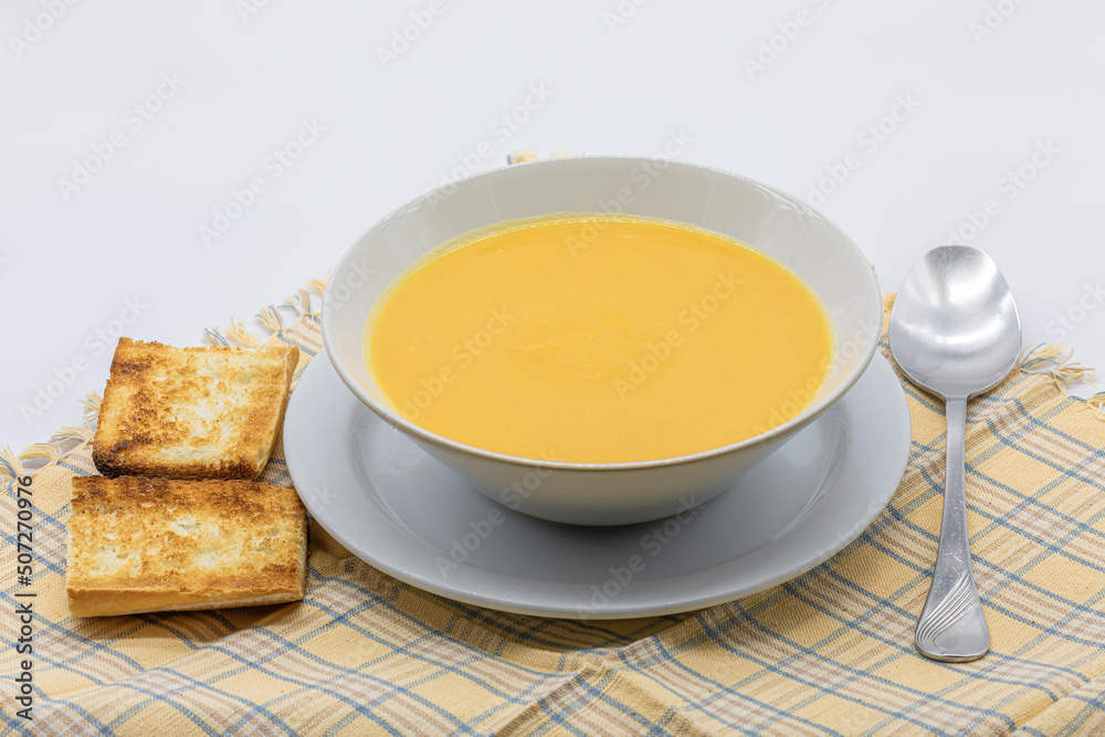 Traditional cream soup made from pumpkin and carrots with toasted bread in a ceramic bowl Traditional cream soup made from pumpkin and carrots with toasted bread in a ceramic bowl