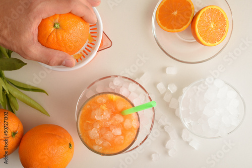 Man preparing orange juice with ice on white table detail