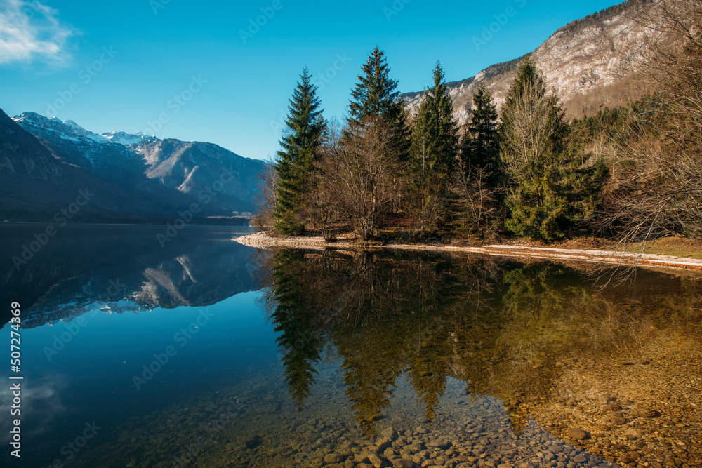 Obraz premium Autumn landscape by the lake Bohinj in Julian Alps. Fascinating reflectins in the lake on a cloudy day.