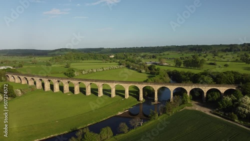 View along Arthington viaduct and river Wharfe with people walking in the fields near Otley in the Yorkshire countryside. Drone aerial