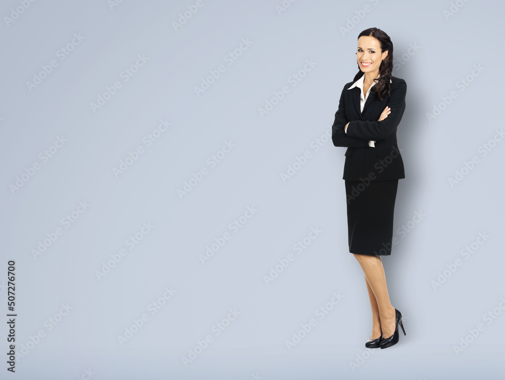 Full body length of happy smiling businesswoman with crossed arms, with copy space area for some text. Confident woman in black suit standing on grey background. Business concept.
