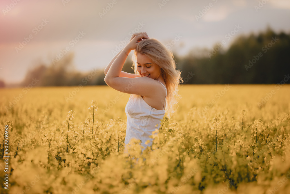 Uśmiechnięta dziewczyna w białej sukience na polu żółtych kwiatów - obrazy, fototapety, plakaty 