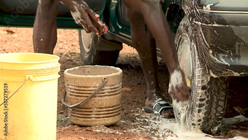 African man washing the car with a sponge and soap. Close-up of hands and wheel.