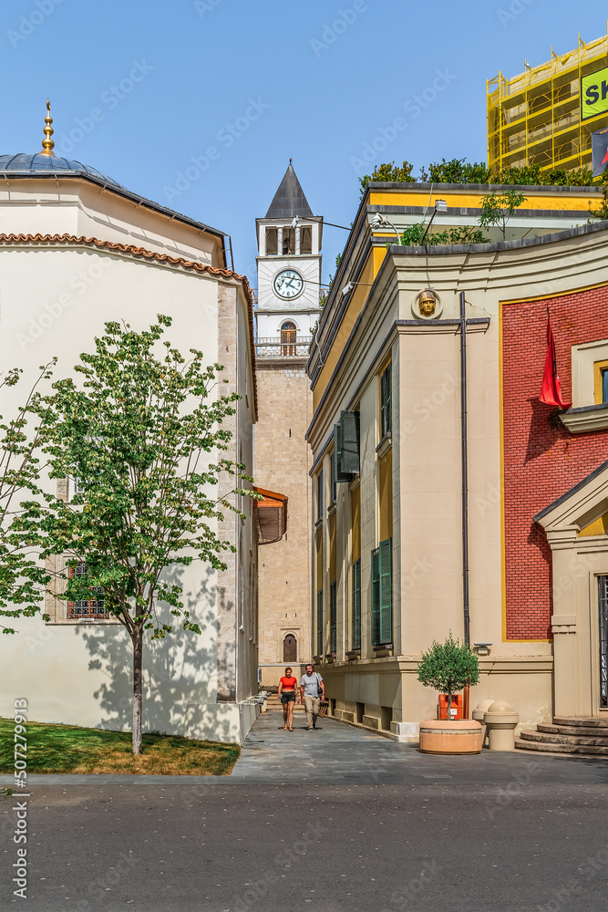 Obraz na płótnie Tirana, Albania - June 21, 2021: View of the Clock Tower between the buildings of Ethem Bey Mosque and Tirana City Hall. Ancient architecture in the center of the Albanian capital w salonie