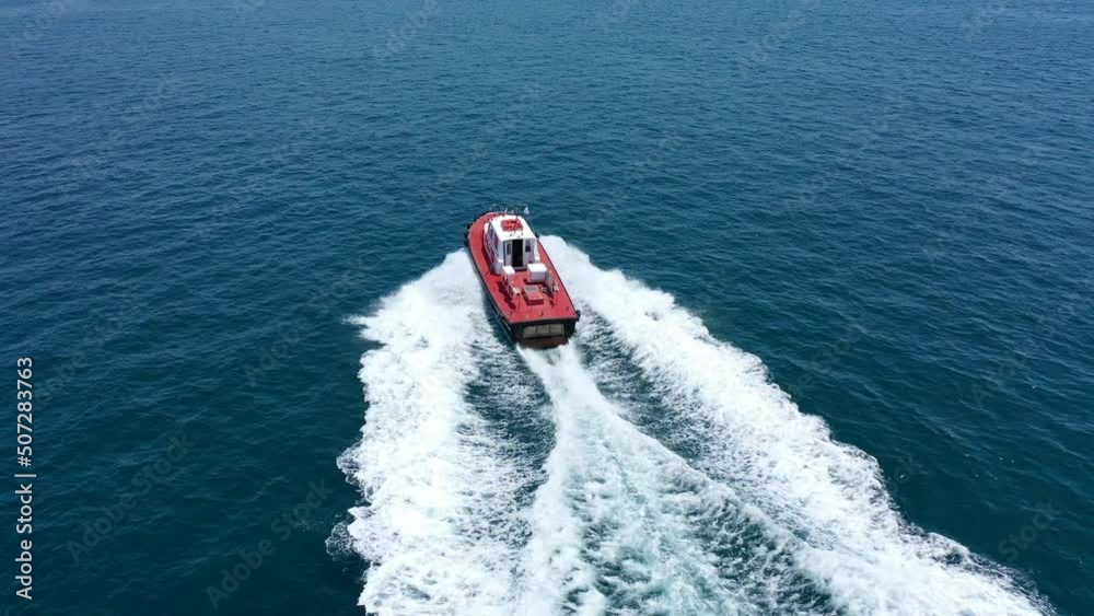 Aerial drone tracking video of red pilot boat cruising in high speed in Mediterranean deep blue sea offering navigational aid to ships