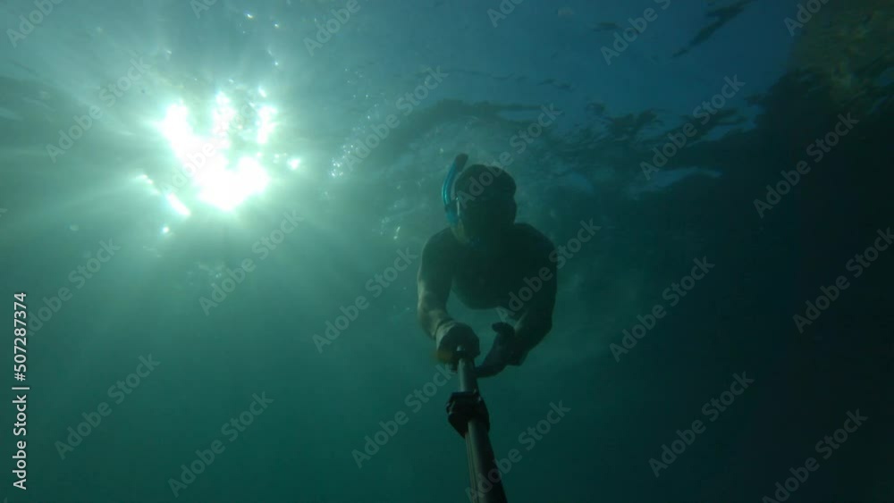 silhouette of a man snorkeling and taking a selfie on a background of bright yellow sun shining from behind. Contrasting rays of the sun under the water illuminating the silhouette of a man immersed silhouette of a man snorkeling and taking a selfie on a background of bright yellow sun shining from behind. Contrasting rays of the sun under the water illuminating the silhouette of a man immersed