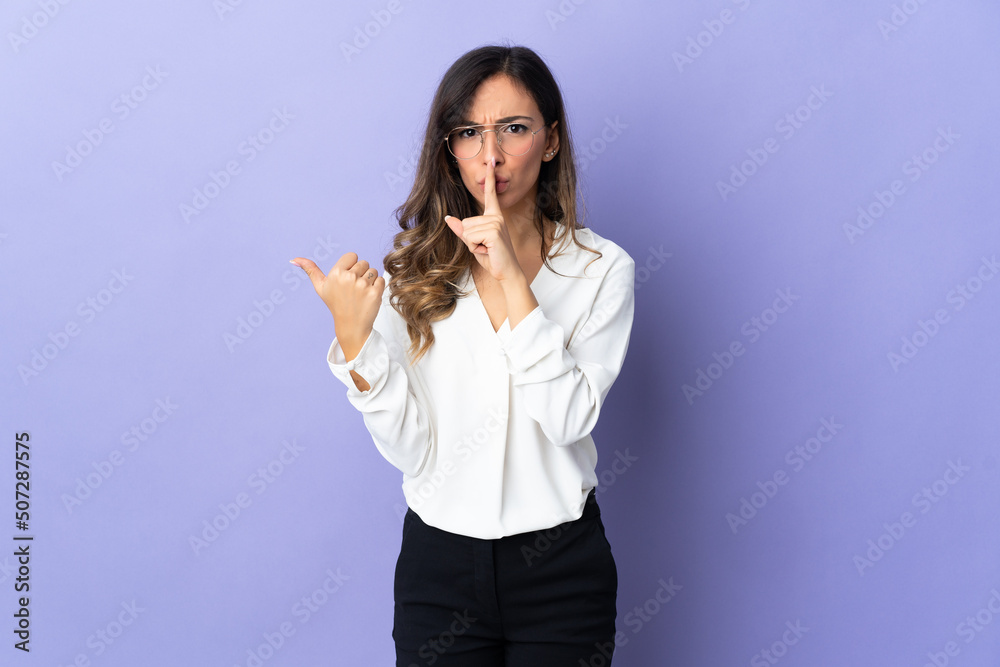 Young caucasian woman isolated on purple background pointing to the side and doing silence gesture Young caucasian woman isolated on purple background pointing to the side and doing silence gesture
