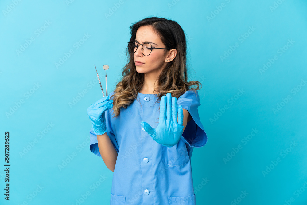 Woman dentist holding tools over isolated on blue background making stop gesture and disappointed Woman dentist holding tools over isolated on blue background making stop gesture and disappointed