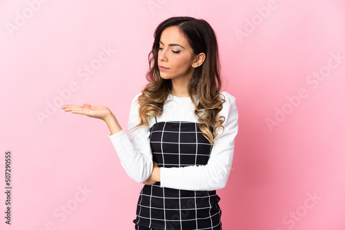 Young caucasian woman isolated on pink background holding copyspace with doubts © luismolinero