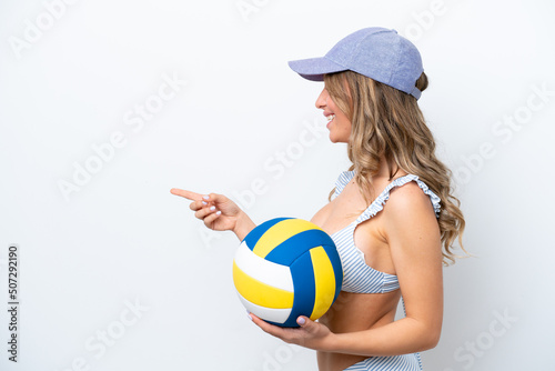 Young woman playing volleyball wearing a swimsuit isolated on white background pointing to the side to present a product