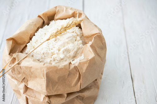 Wheat flour in paper pack with ears of wheats on white wooden table.