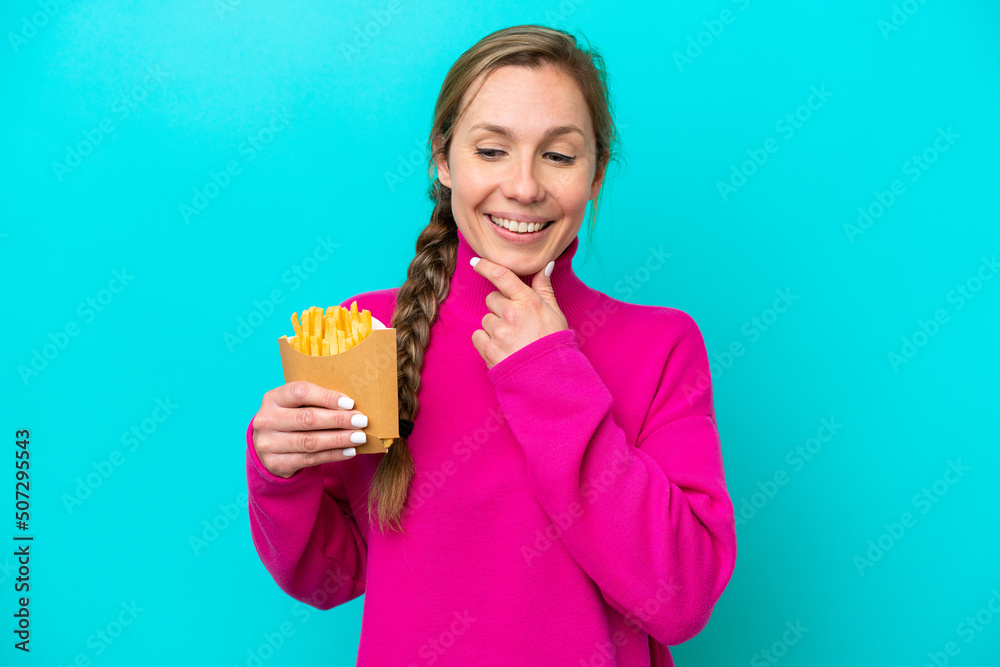 Young caucasian woman holding fried chips isolated on blue background looking to the side and smiling Young caucasian woman holding fried chips isolated on blue background looking to the side and smiling