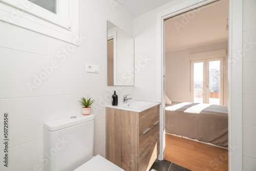 Bathroom with wooden cabinet with white porcelain sink  square frameless mirror and access to a bedroom with terrace
