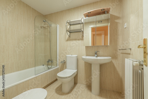Bathroom with cabinet doors with mirror  porcelain sink with the same material  bathtub with glass screen and ceramic tiles