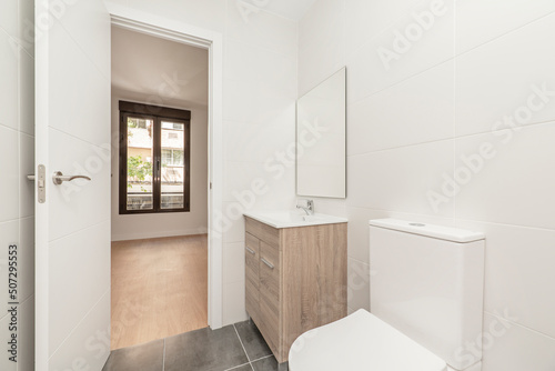 Bathroom with wooden cabinet with drawers  white porcelain sink  square frameless mirror  glass shower stall and white tiles