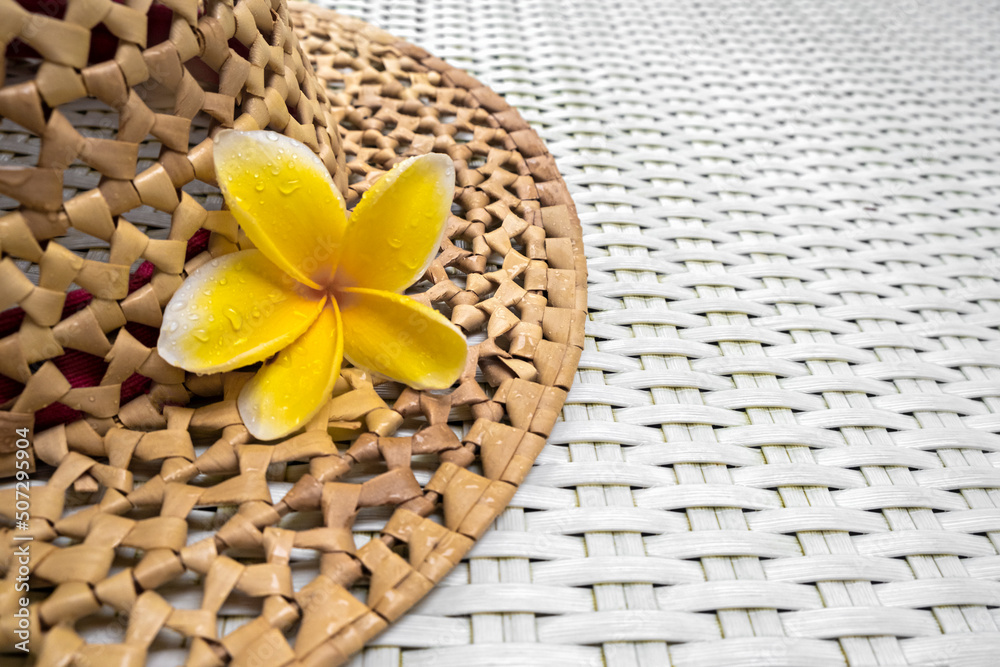 Travel. Summer mockup. Straw hat on a white textured background with a frangipani flower. Side view close-up. Holidays concept , vacations and holidays.