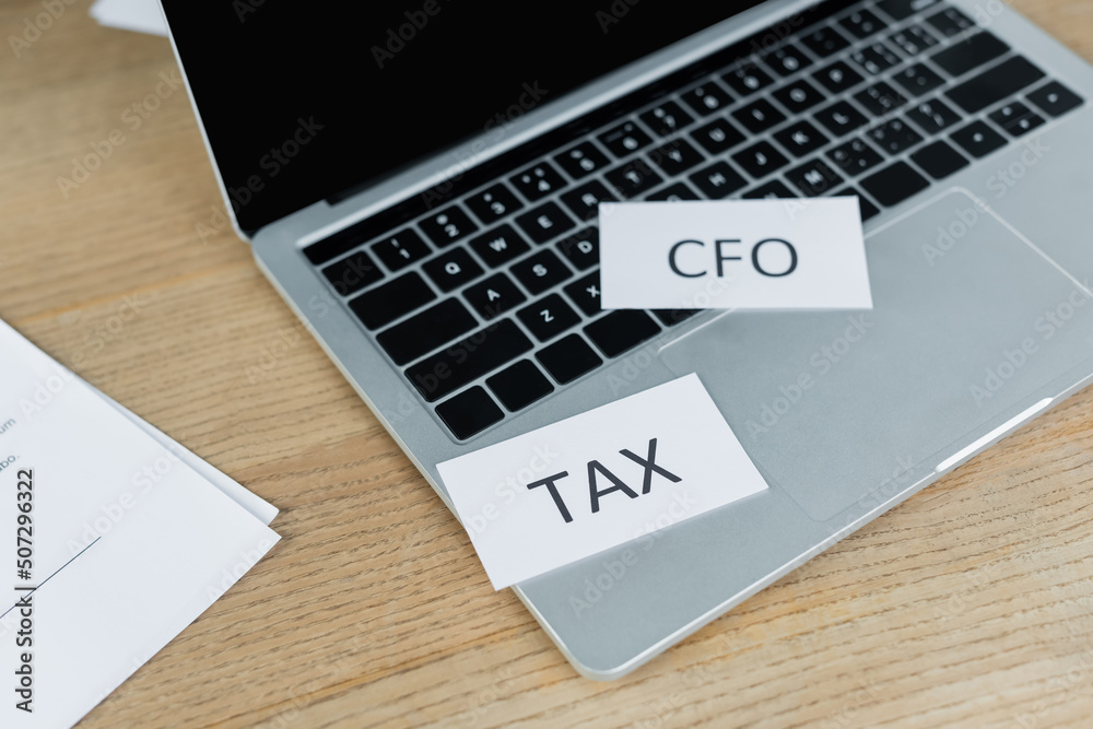 papers with tax and cfo lettering near laptop with blank screen. papers with tax and cfo lettering near laptop with blank screen.
