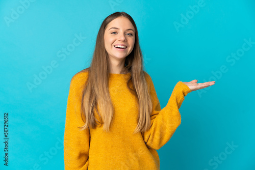 Young Lithuanian woman isolated on blue background holding copyspace imaginary on the palm to insert an ad