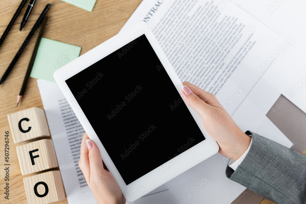 cropped view of businesswoman holding digital tablet with blank screen above papers with contract and cfo letters on cubes. cropped view of businesswoman holding digital tablet with blank screen above papers with contract and cfo letters on cubes.