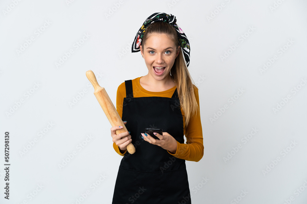 Young Lithuanian woman holding a rolling pin isolated on white background surprised and sending a message Young Lithuanian woman holding a rolling pin isolated on white background surprised and sending a message