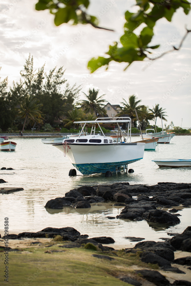 Fototapeta premium Yachts and fishing boats on the shore with black large stones with mountain range in the background