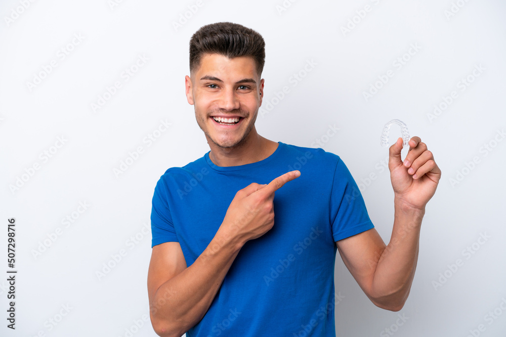 Young caucasian man holding invisible braces isolated on white background and pointing it Young caucasian man holding invisible braces isolated on white background and pointing it