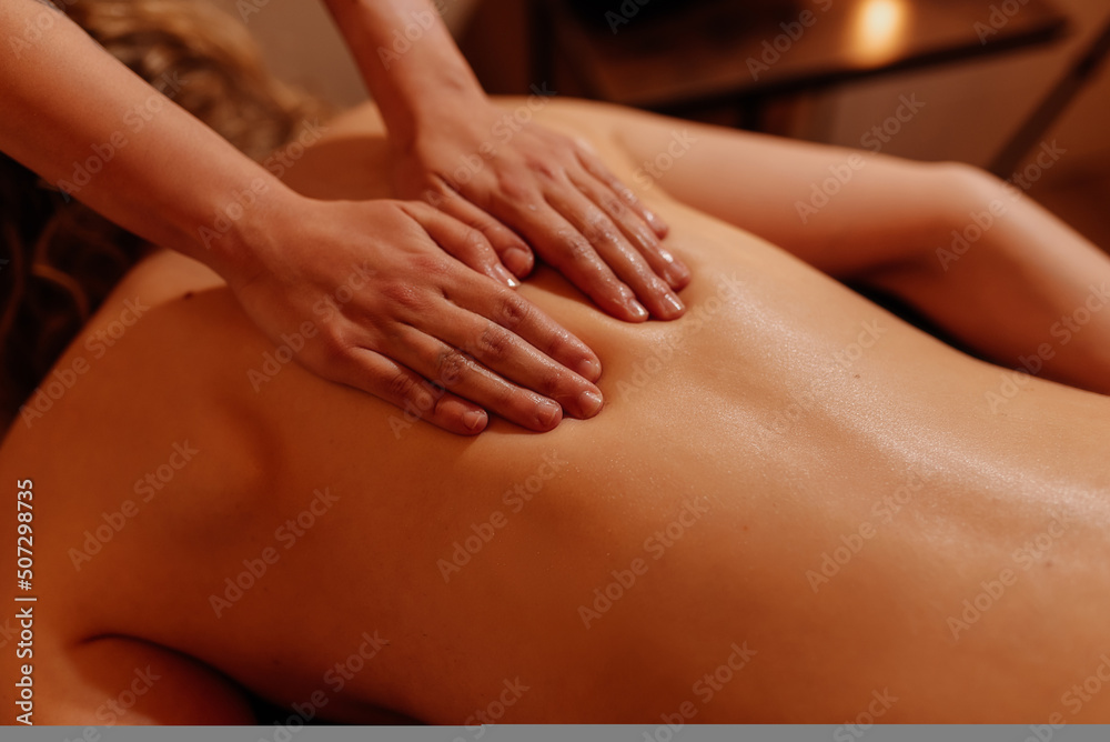 close-up hands of unrecognizable person performing a back massage on a caucasian woman in a beauty and wellness center with dim light.