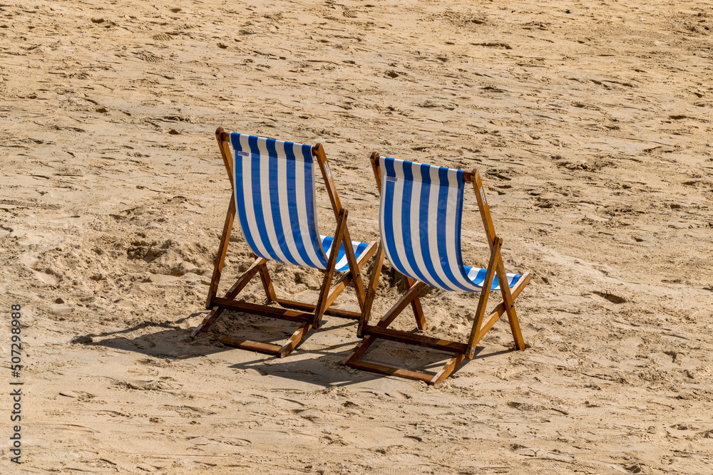 Two blue and white striped deckchairs on a beach