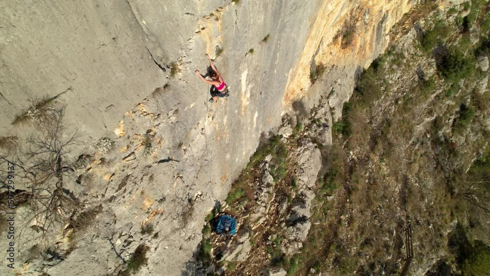 AERIAL: Sporty young woman lead climbing and using quickdraw to attach rope. Female rock climber in the middle of limestone climbing wall. Adrenaline sport activities in beautiful outdoor environment. AERIAL: Sporty young woman lead climbing and using quickdraw to attach rope. Female rock climber in the middle of limestone climbing wall. Adrenaline sport activities in beautiful outdoor environment.