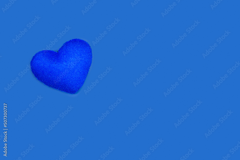 Fotografie Un corazón azul de fieltro hecho a mano sobre un fondo azul liso y aislado