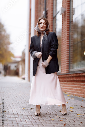 fashion young woman in dress with hairstyle wearing in polka dots shawl and gloves with makeup posing outside. Brunette woman in dark jacket outdoors looks in camera