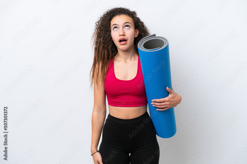 Young sport Arab woman going to yoga classes while holding a mat isolated on white background looking up and with surprised expression Young sport Arab woman going to yoga classes while holding a mat isolated on white background looking up and with surprised expression