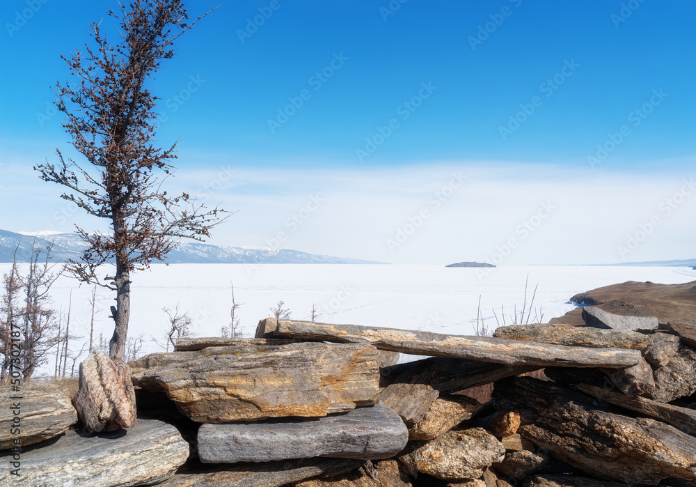 Winter landscape with mountains and dark blue ice of Baikal Lake in Siberia with clear blue sky. Natural background.