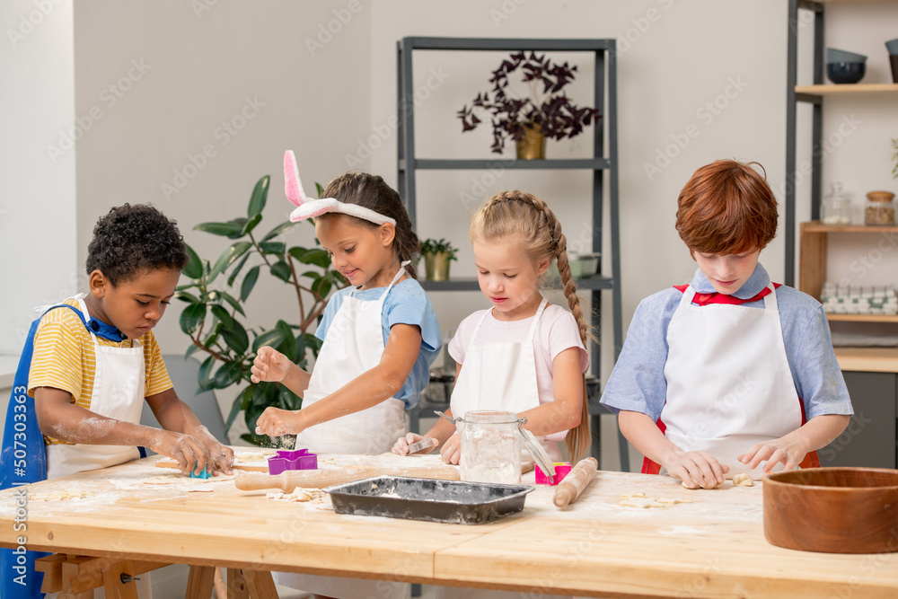 Group of little kids cooking cookies over tray on kitchen table covered with flour Group of little kids cooking cookies over tray on kitchen table covered with flour