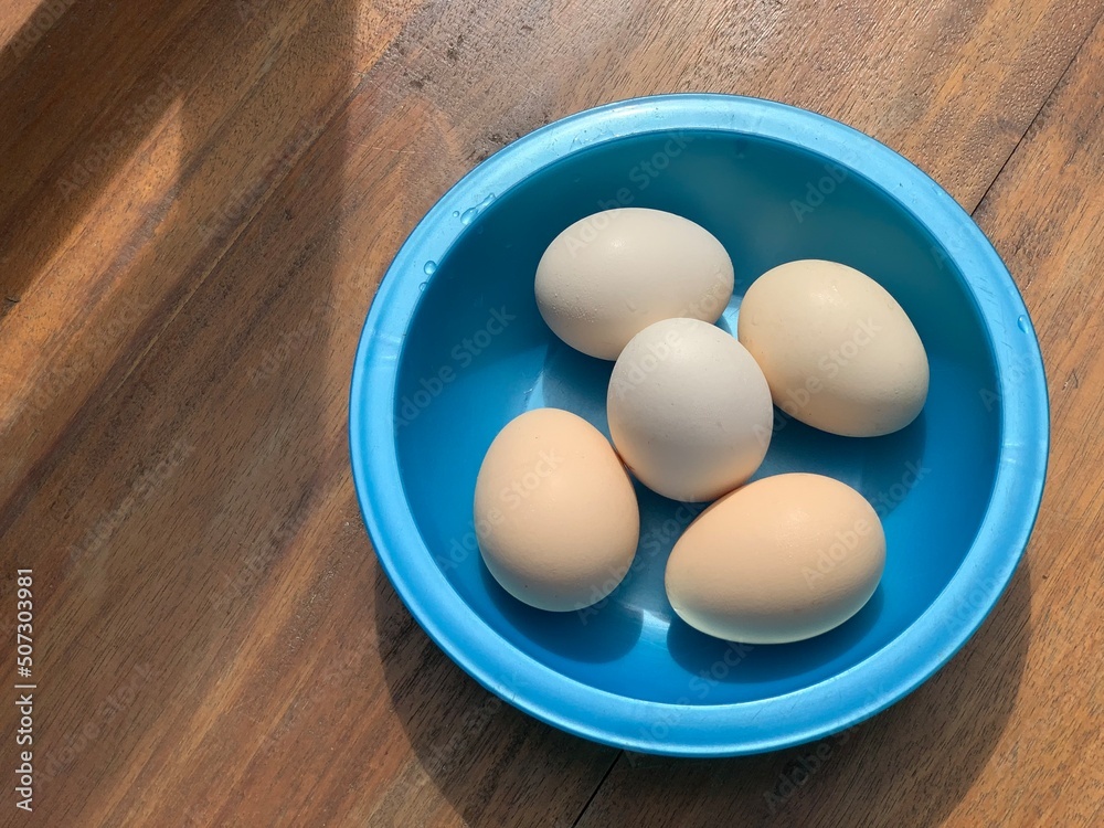 top view shot of eggs in a blue plastic bowl on a wooden table top view shot of eggs in a blue plastic bowl on a wooden table