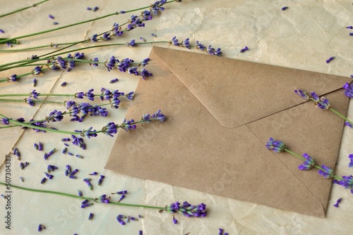 Mockup of craft paper envelope on vintage paper background with lavender flowers close-up. Happy Birthday, Valentine's day, wedding, Mother's Day greeting card concept.