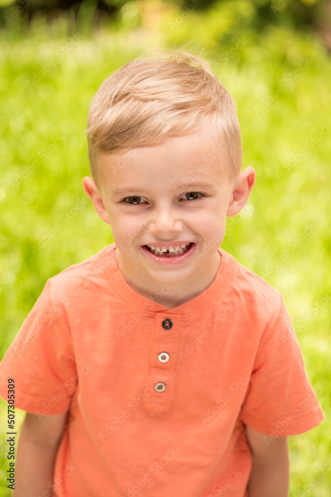five-year-old boy making faces. A five-year-old blond boy makes faces while standing on the street in sunny weather five-year-old boy making faces. A five-year-old blond boy makes faces while standing on the street in sunny weather