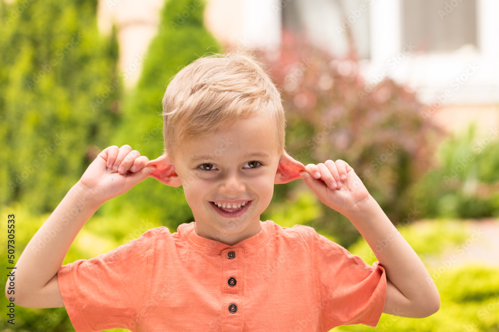 five-year-old boy making faces. A five-year-old blond boy makes faces while standing on the street in sunny weather five-year-old boy making faces. A five-year-old blond boy makes faces while standing on the street in sunny weather