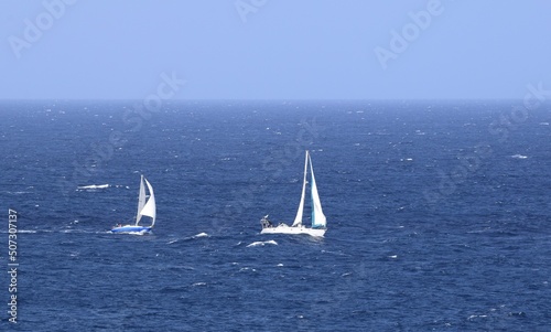 Two sailing yachts with white sails racing on the blue ocean, blue sky in the background