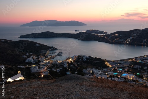 Colorful sunset and view of the illuminated harbor of Ios and the island of Folegandros in the background