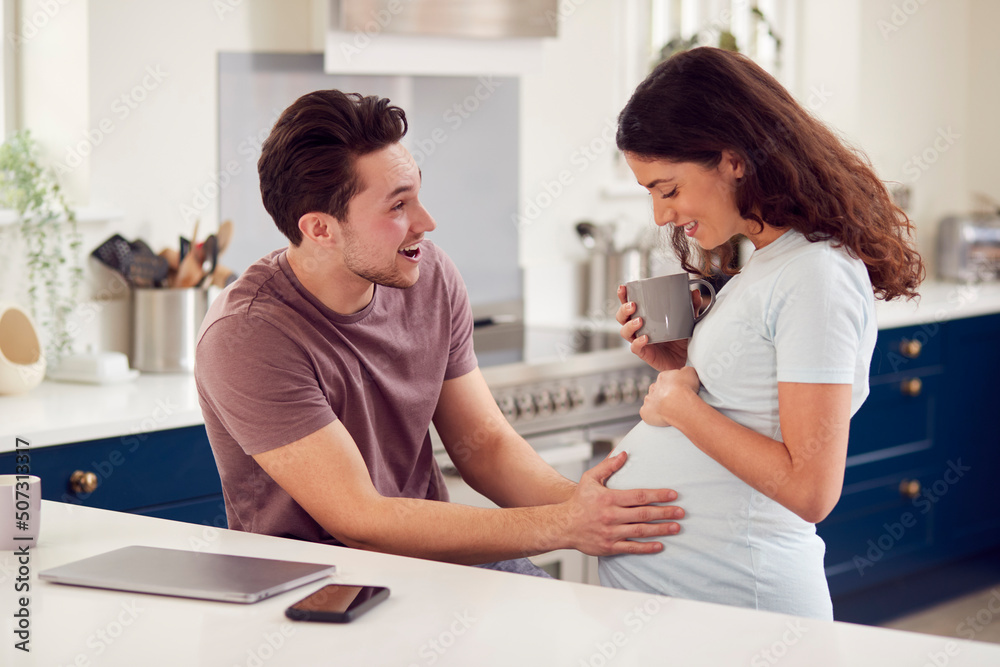 Excited Pregnant Transgender Couple At Home In Kitchen Together With Man Touching Woman's Stomach Excited Pregnant Transgender Couple At Home In Kitchen Together With Man Touching Woman's Stomach