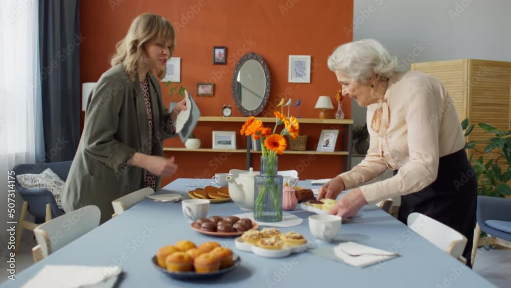 Zoom in shot of young woman helping senior grandmother serving food on table while preparing for holiday dinner at home