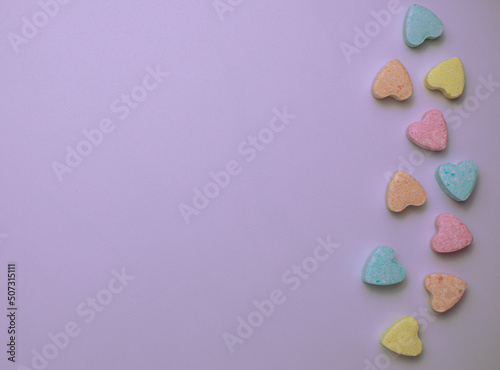Colorful pastel heart-shaped candies on a light purple background © Maria Rzeszotarska