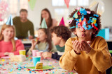 Boy Blowing Confetti At Camera At Birthday Party With Friends And Parents At Home