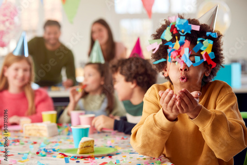 Boy Blowing Confetti At Camera At Birthday Party With Friends And Parents At Home