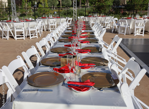 Long party dinner table at an outdoor venue decorated with ivory, red and gold.