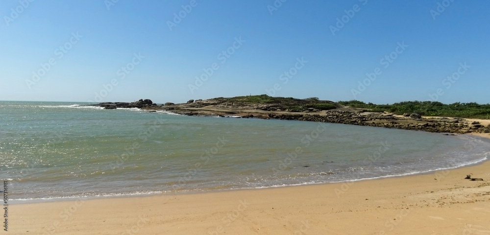 Linda praia, com montanhas ao fundo e céu azul,  localizada em Vitória no estado do Espírito Santo, Brasil.